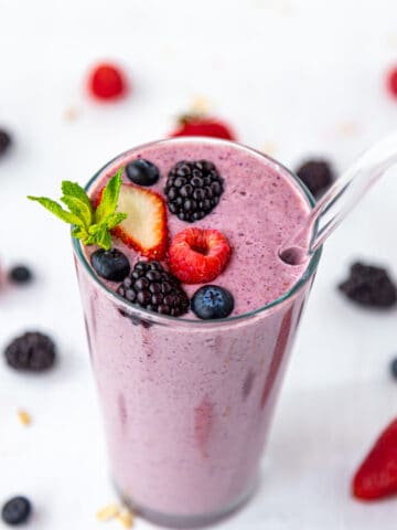 Berry Oat smoothie in a tall glass with glass straw garnished with berries and mint