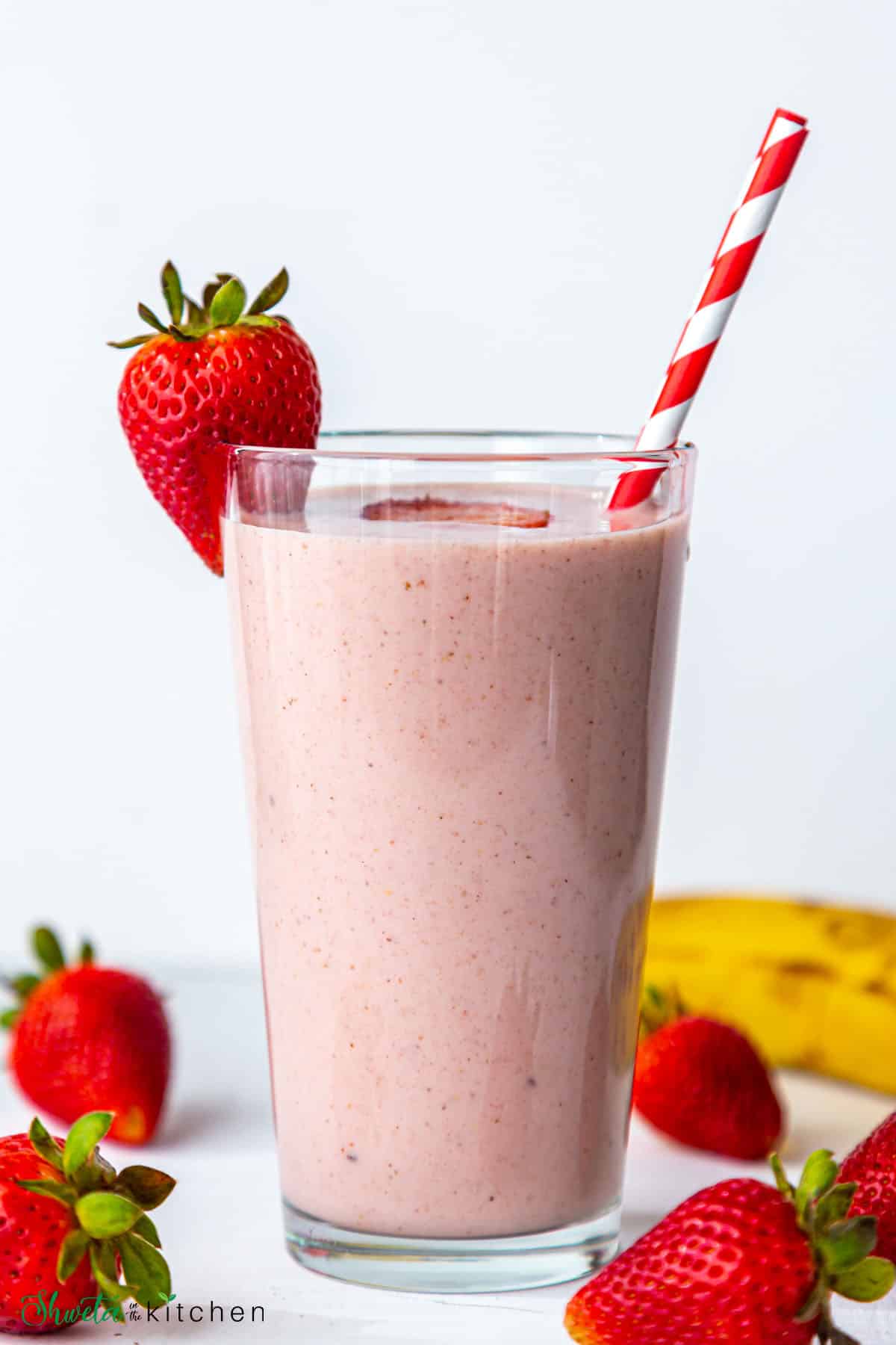 front view of glass of Strawberry banana smoothie with red stripped straw and strawberry on the glass rim