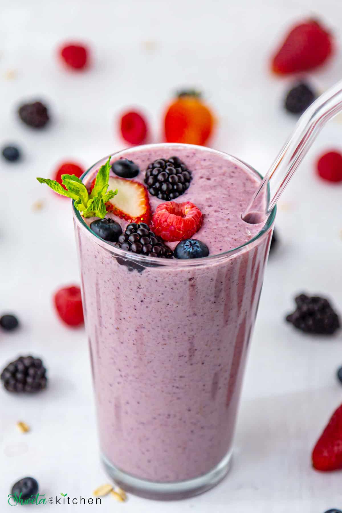 Berry Oat smoothie in a tall glass with glass straw garnished with berries and mint
