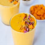 Mango lassi in tall glasses garnished with mangoes and nuts