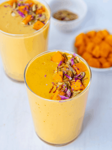 Mango lassi in tall glasses garnished with mangoes and nuts