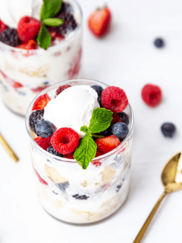 Side view of berry parfait topped with cream and mint and golden spoon on side