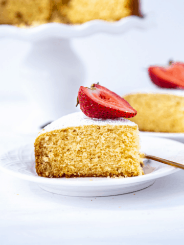 Slice of eggless vanilla cake dusted with sugar and topped with strawberry