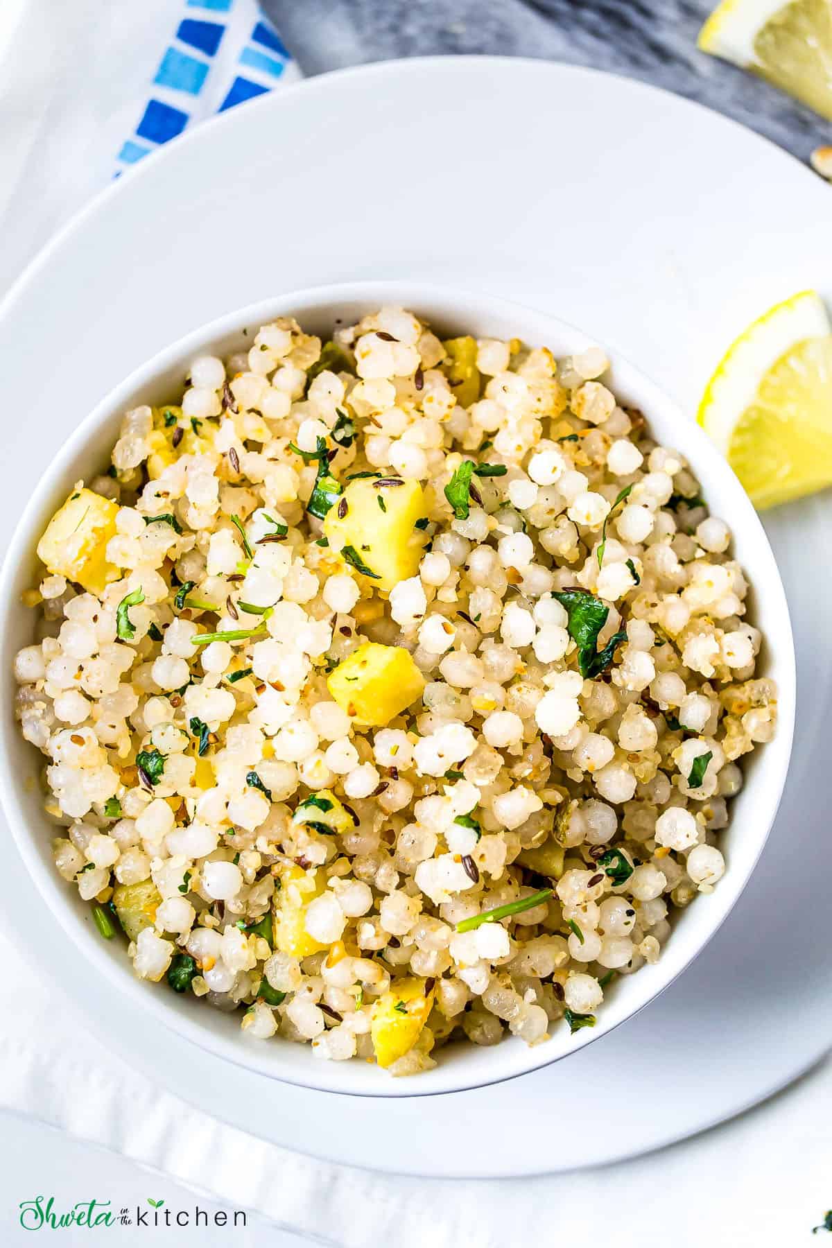 Sabudana Khichdi served in a white bowl on a plate with a slice of lemon