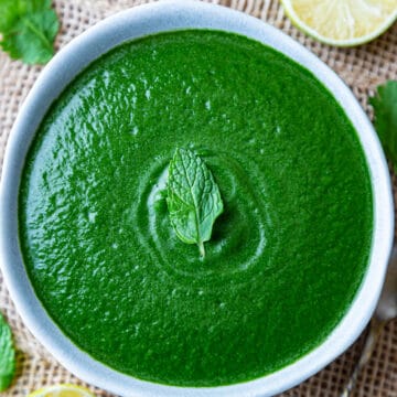 Cilantro Mint Chutney served in a bowl placed on wooden surface with cut lemons on side.