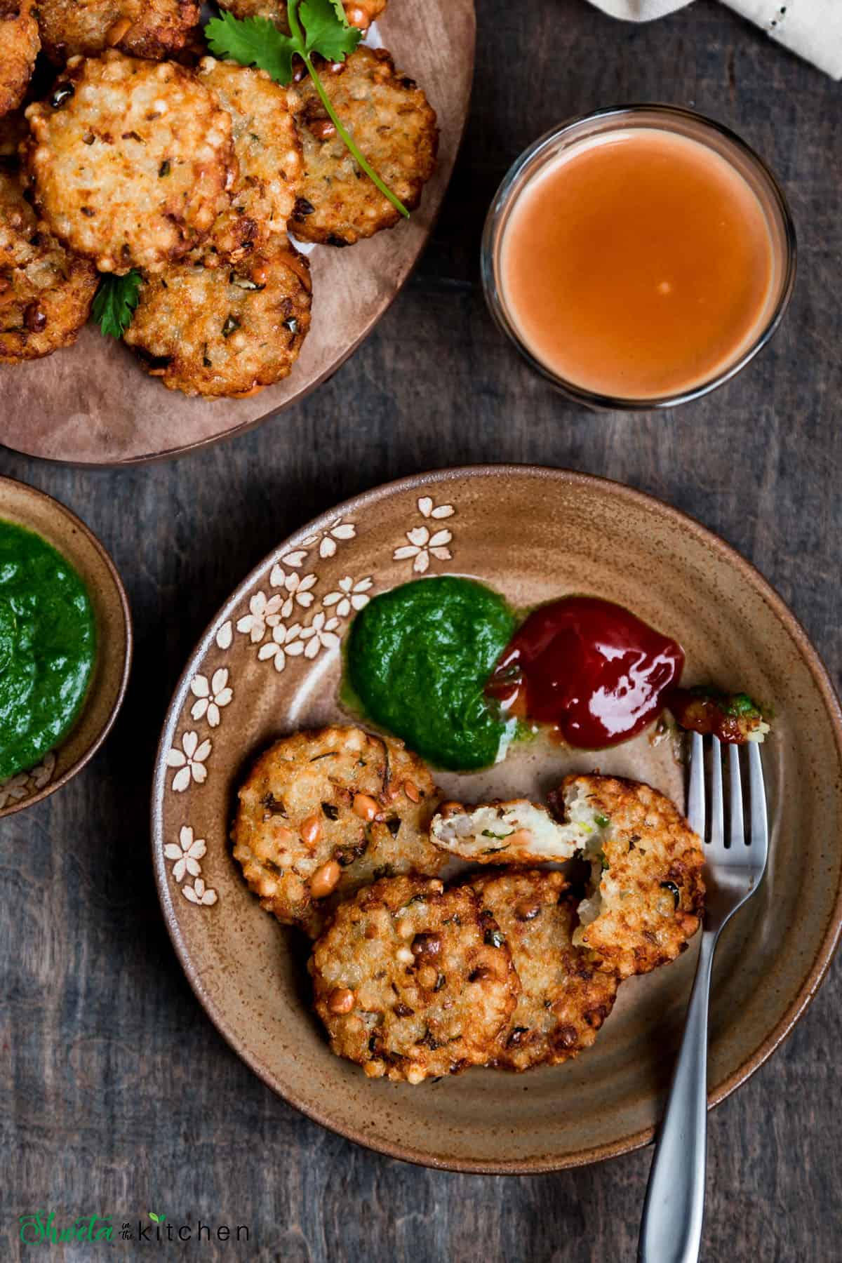 Four sabudana vada served on a plate with a spoonful of green chutney and ketchup