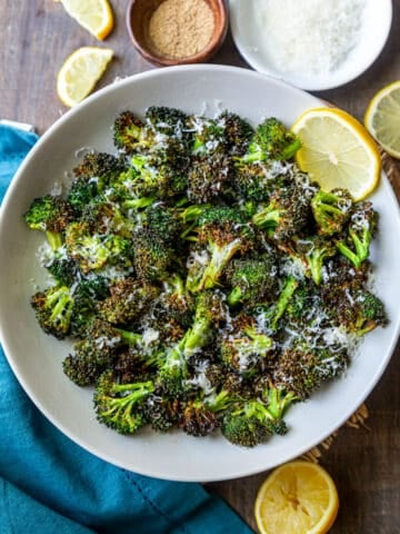 Air fryer broccoli on a white plate with lemon and parmesan on the side