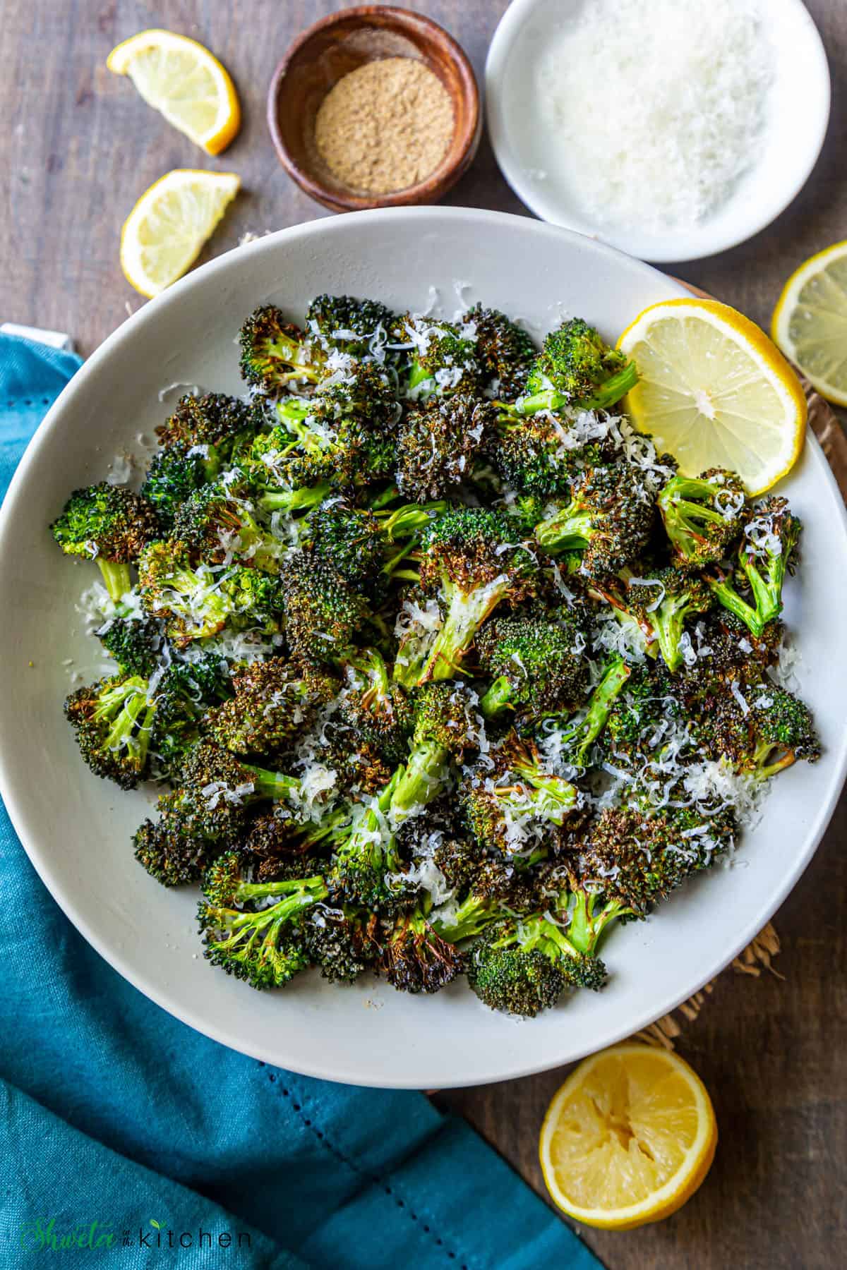 Air fryer broccoli on a white plate with lemon and parmesan on the side