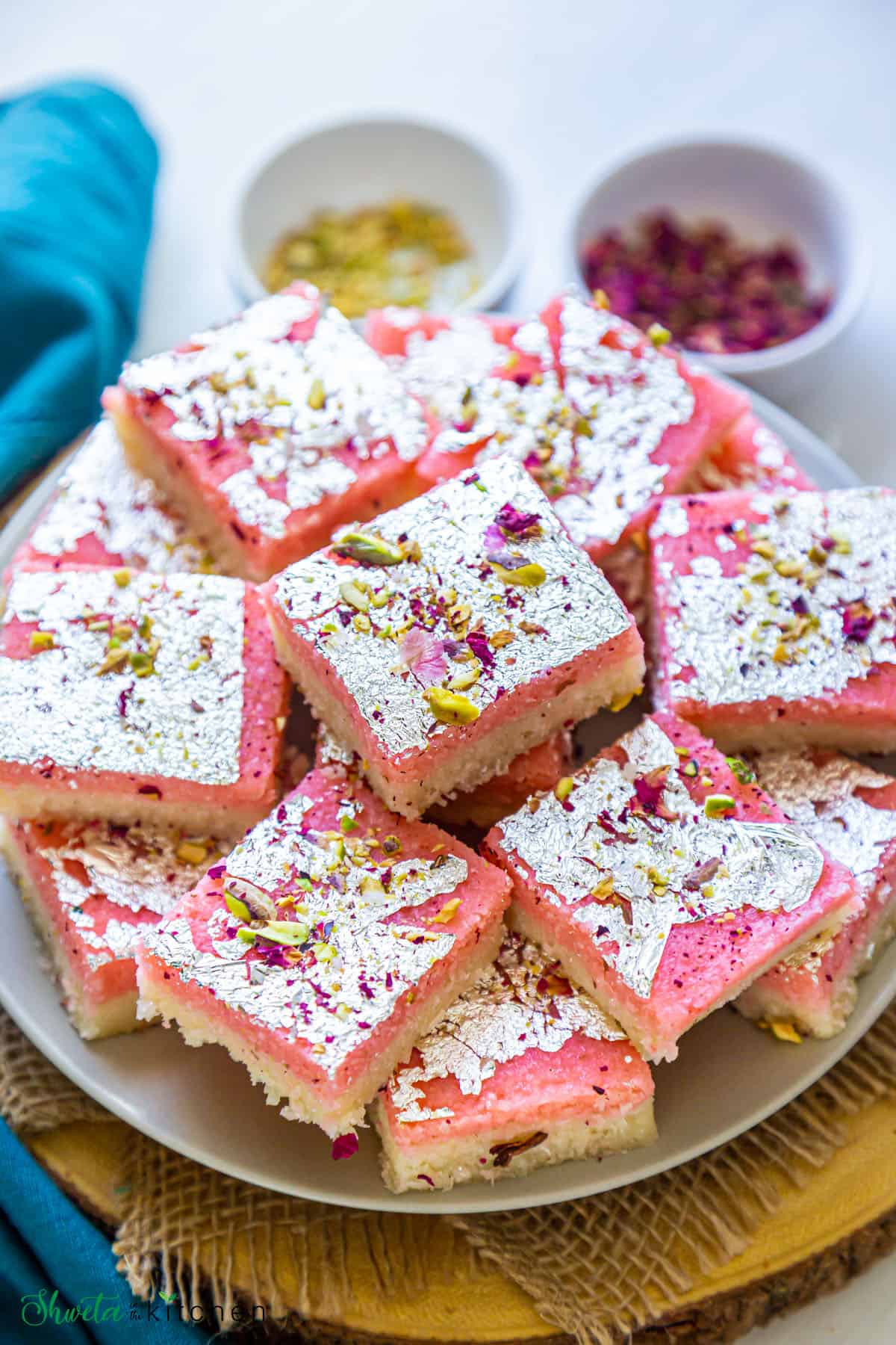 Coconut Burfi garnished with pistachios and rose petals arranged in circular pattern on a plate
