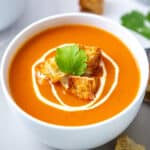 Creamy Vegan Tomato soup served in a white bowl with a swirl of cream and croutons.