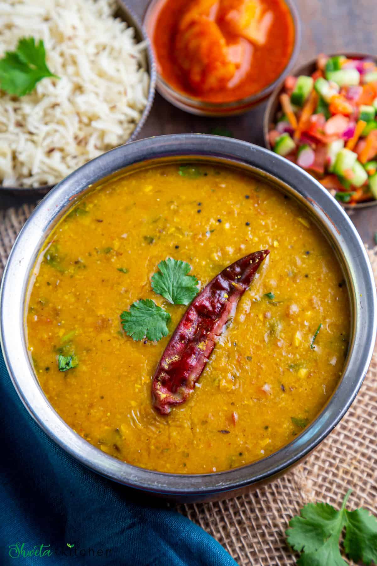 Side angle shot of Dal Fry in a round dish with rice, salad and pickle on side