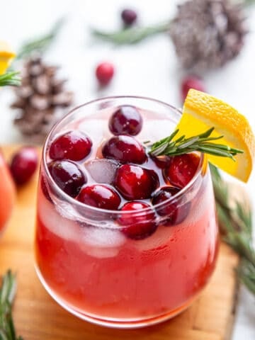 Christmas Punch in a glass garnished with cranberries, orange slice and rosemary