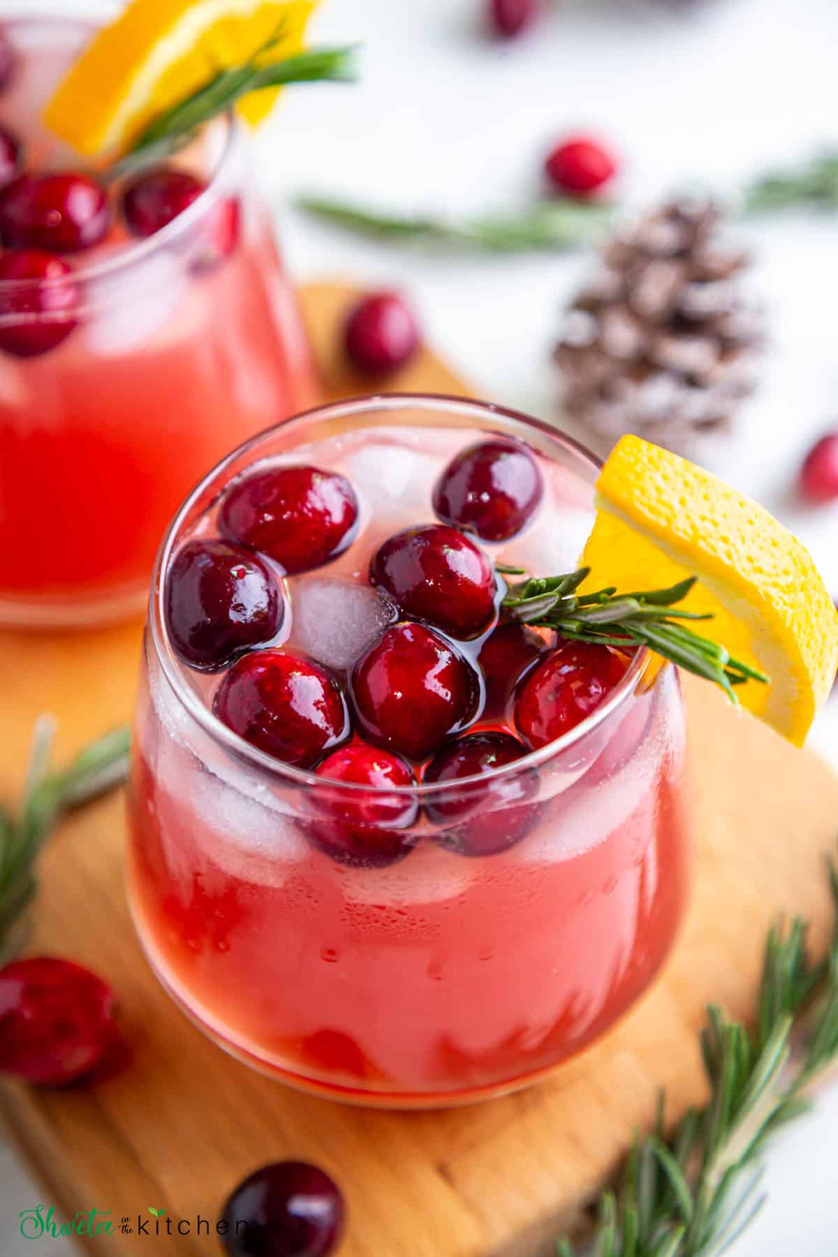 Side view of Easy Christmas Punch in a glass garnished with cranberries, orange slice and rosemary