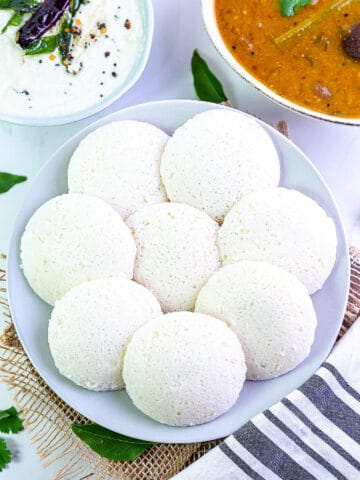 8 idli on a plate arranged in circle with chutney and sambar on side