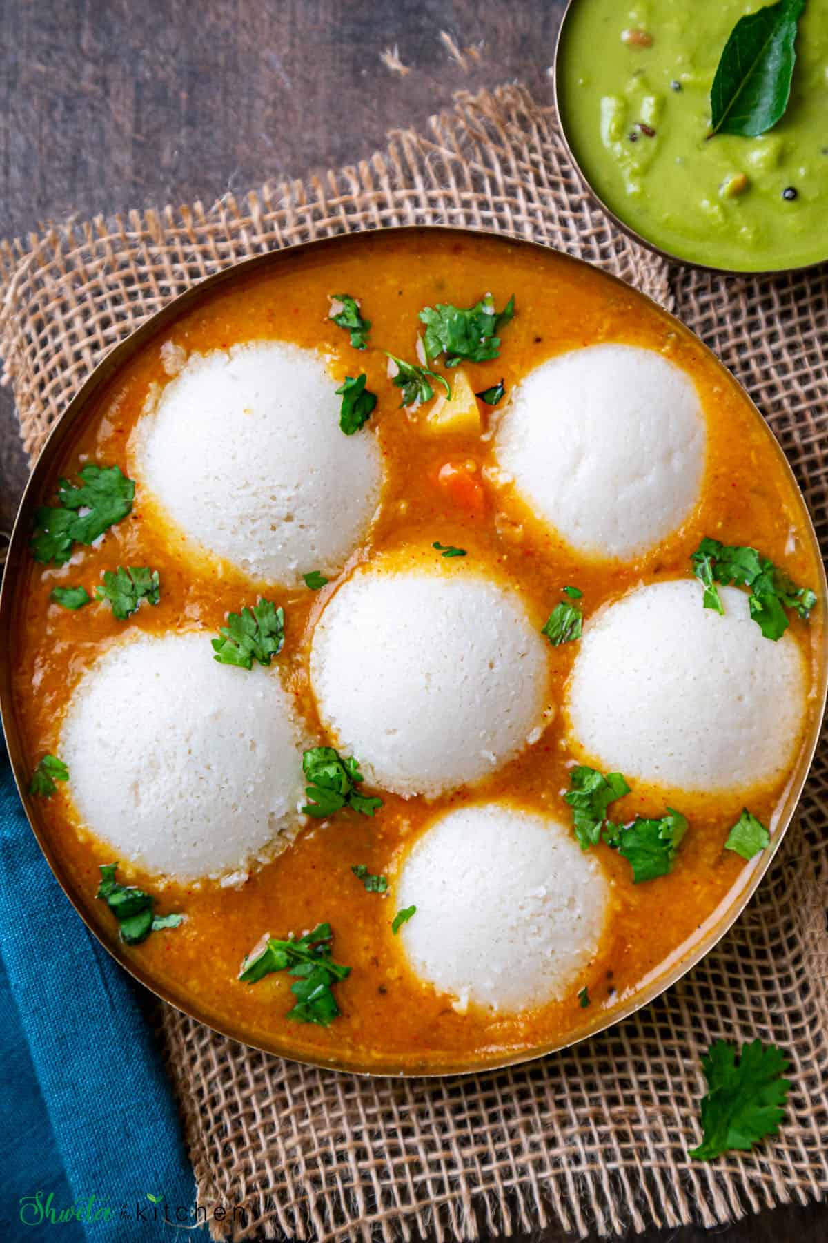 Bowl with 6 Idli dunked in sambar with chutney bowl on the side