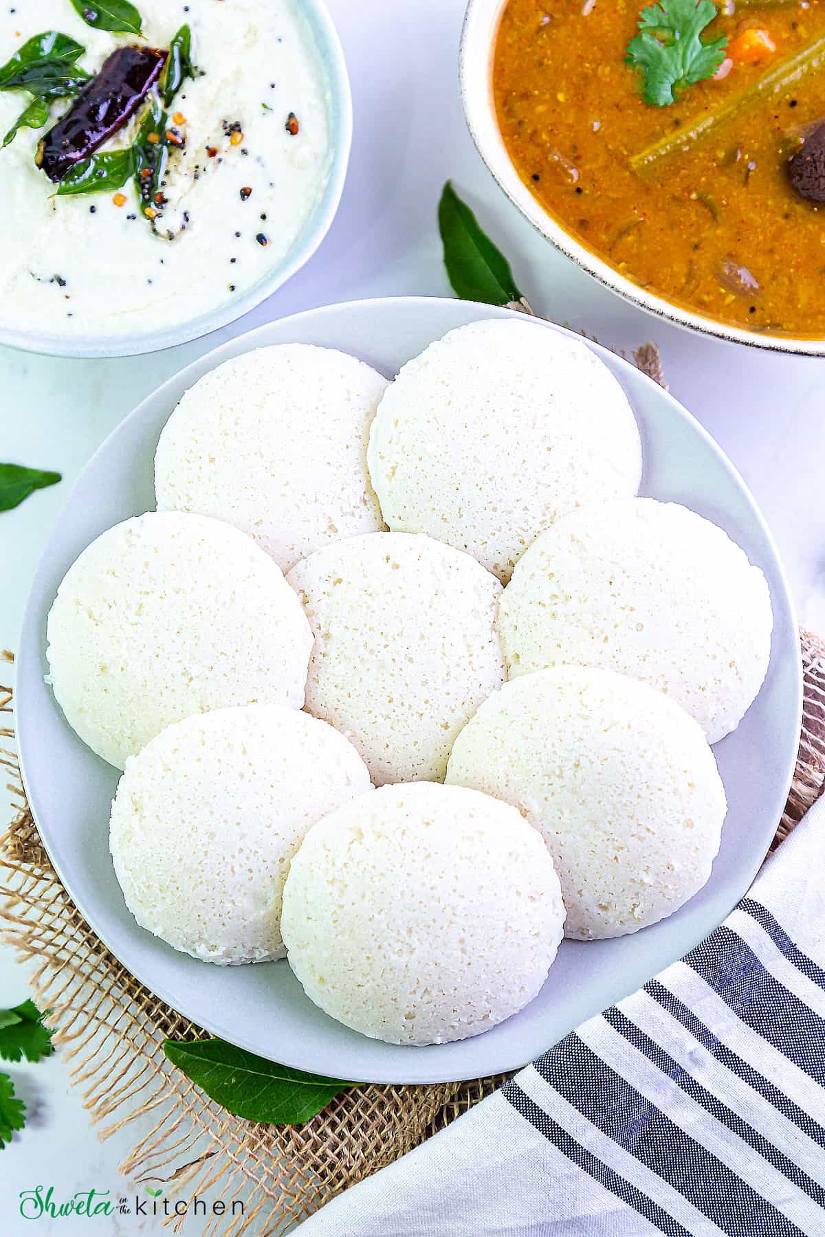 8 idli on a plate arranged in circle with chutney and sambar on side