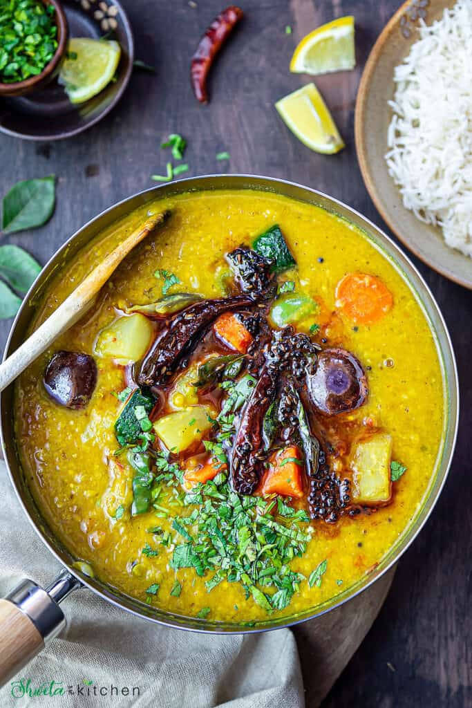 Pot of Instant pot sambar with bowl of rice, lemons and cilantro on the side