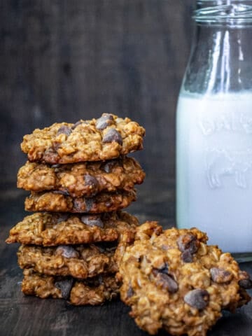 A stack of chocolate oatmeal cookies in front of a bottle of milk