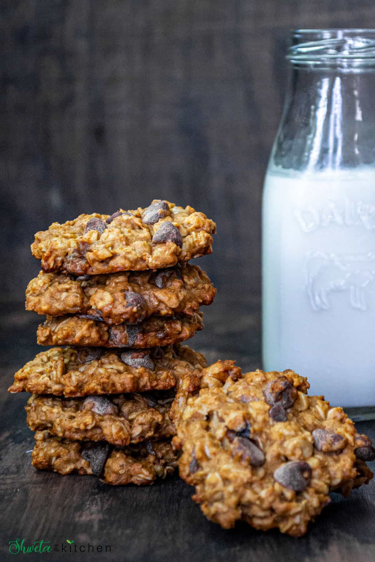 A stack of chocolate oatmeal cookies in front of a bottle of milk