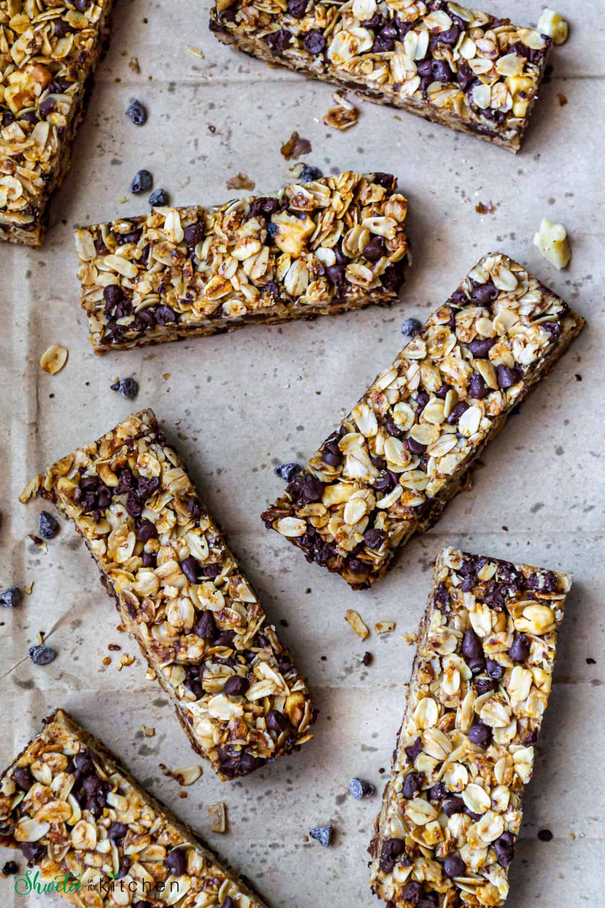 Chewy chocolate chip granola bars scattered on brown paper with bits of chocolate chips and walnuts