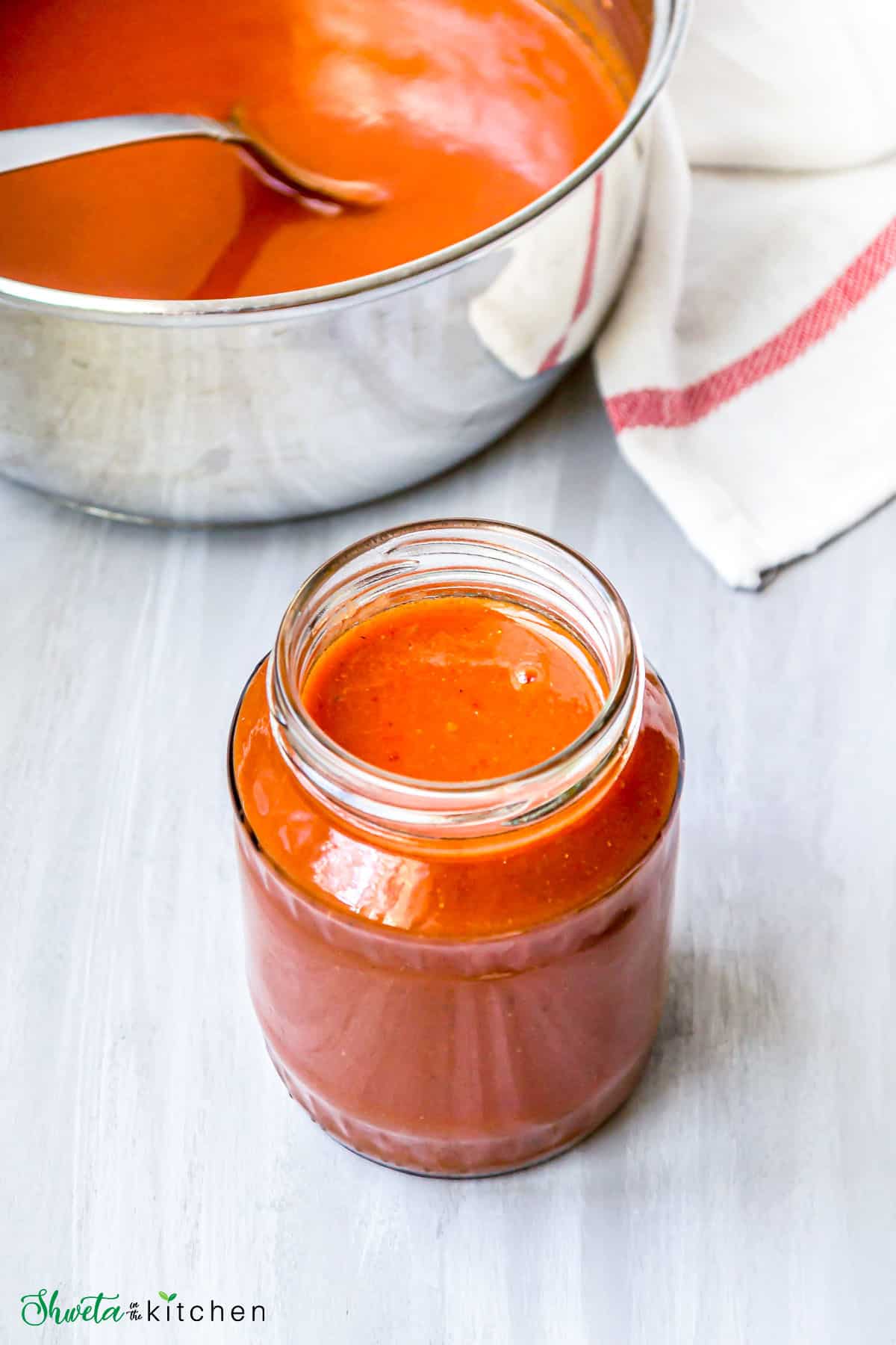 A jar of red enchilada sauce in front of a pot with the sauce