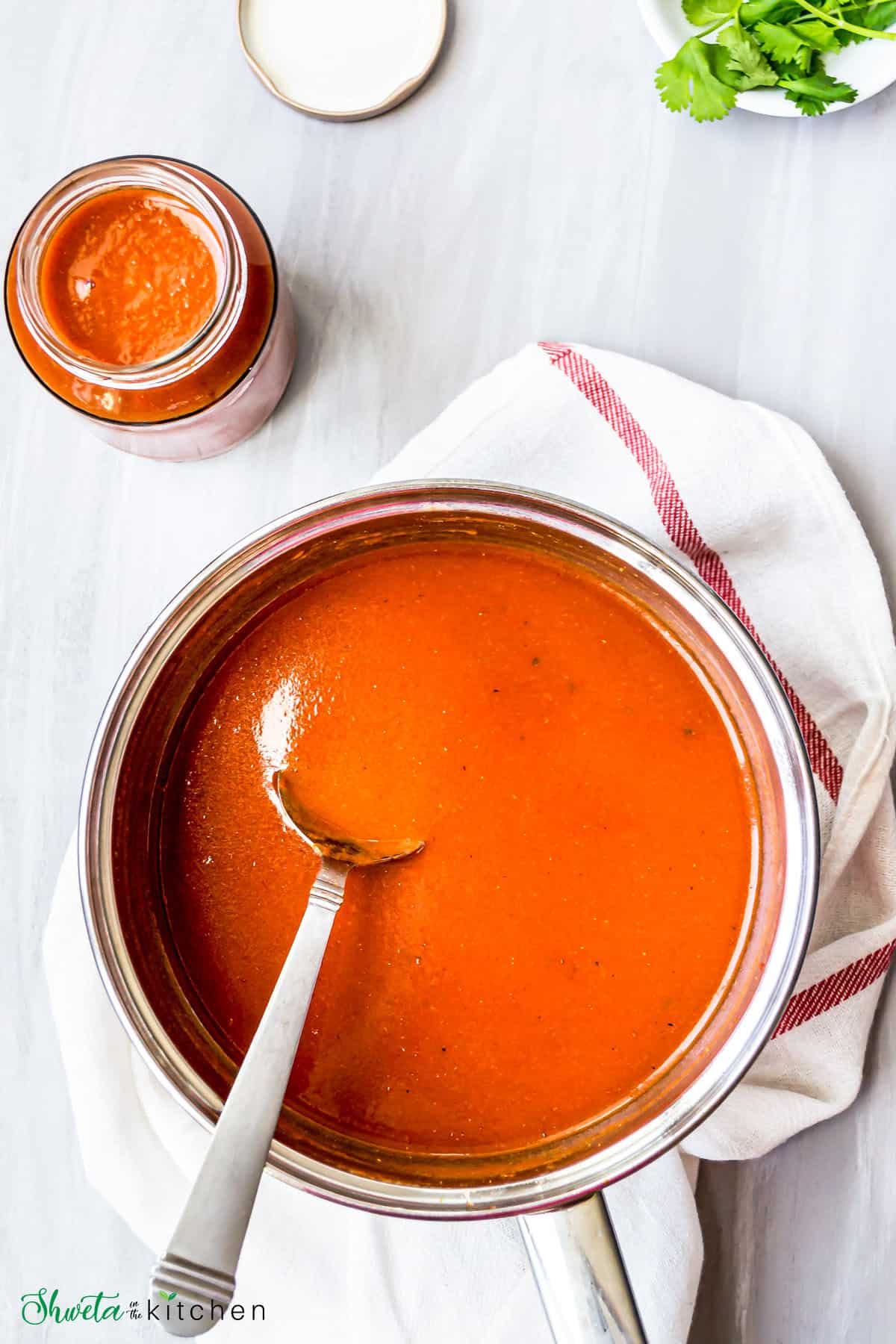 A spoon in a pot of the sauce on top of a white kitchen towel