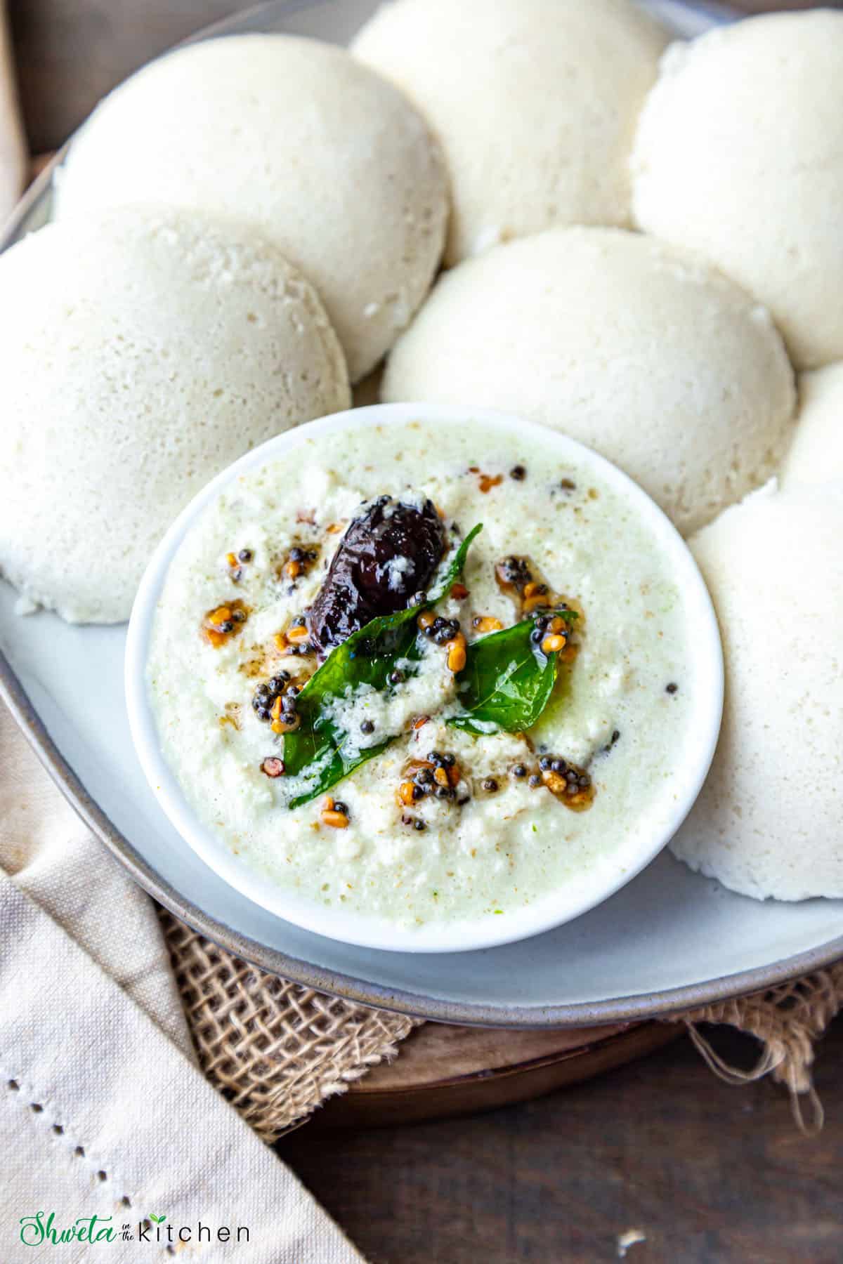Bowl of coconut chutney with tempering on a plate full of idli