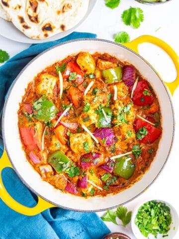 Kadai Paneer in a yellow pot (kadai) with naan, salad and ginger juliennes on side