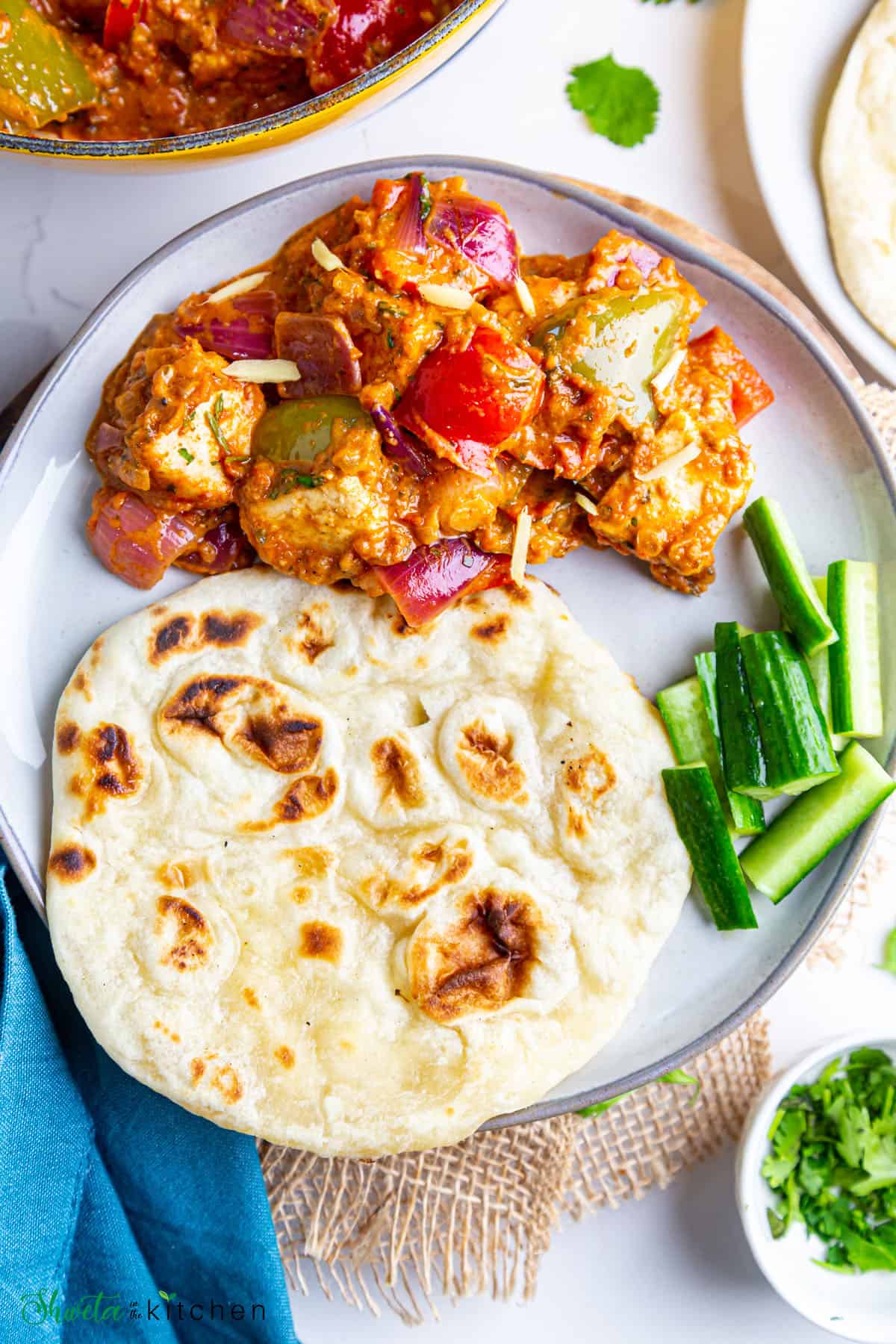 Plate with restaurant style kadai paneer, naan and cut cucumbers