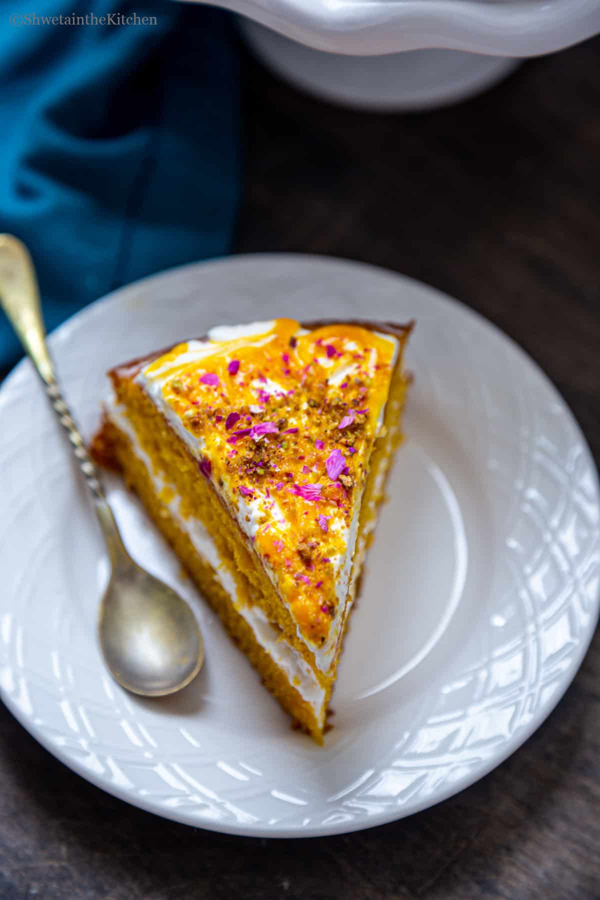 Slice of eggless mango cake on a plate with spoon on the side