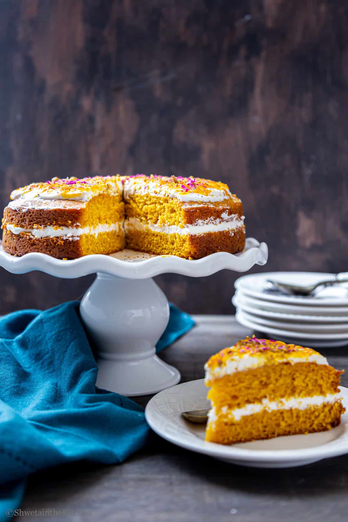 Front view of Mango cake placed on a cake stand with slice cut and placed on a plate