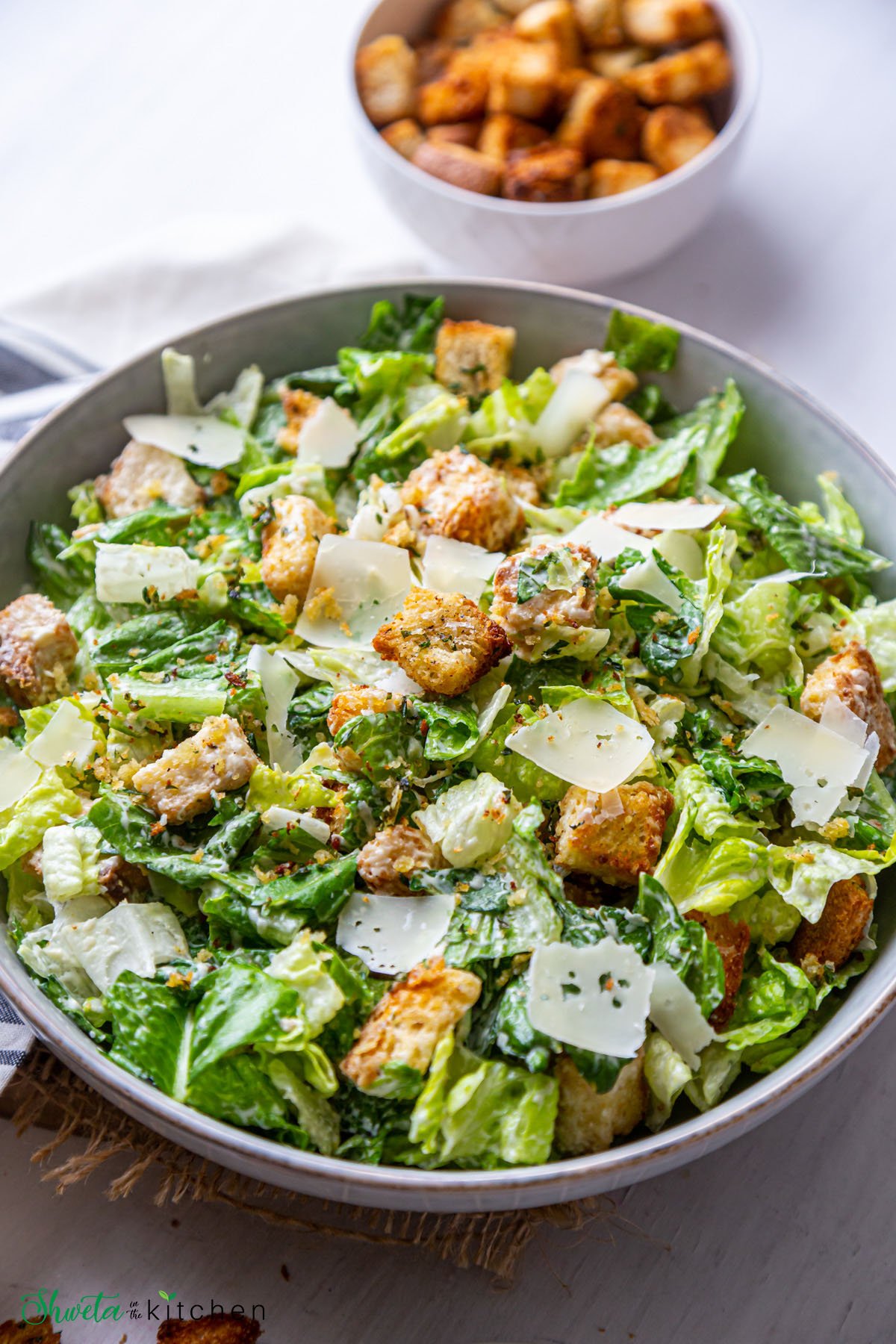 Side view of vegetarian caesar salad bowl with croutons in background