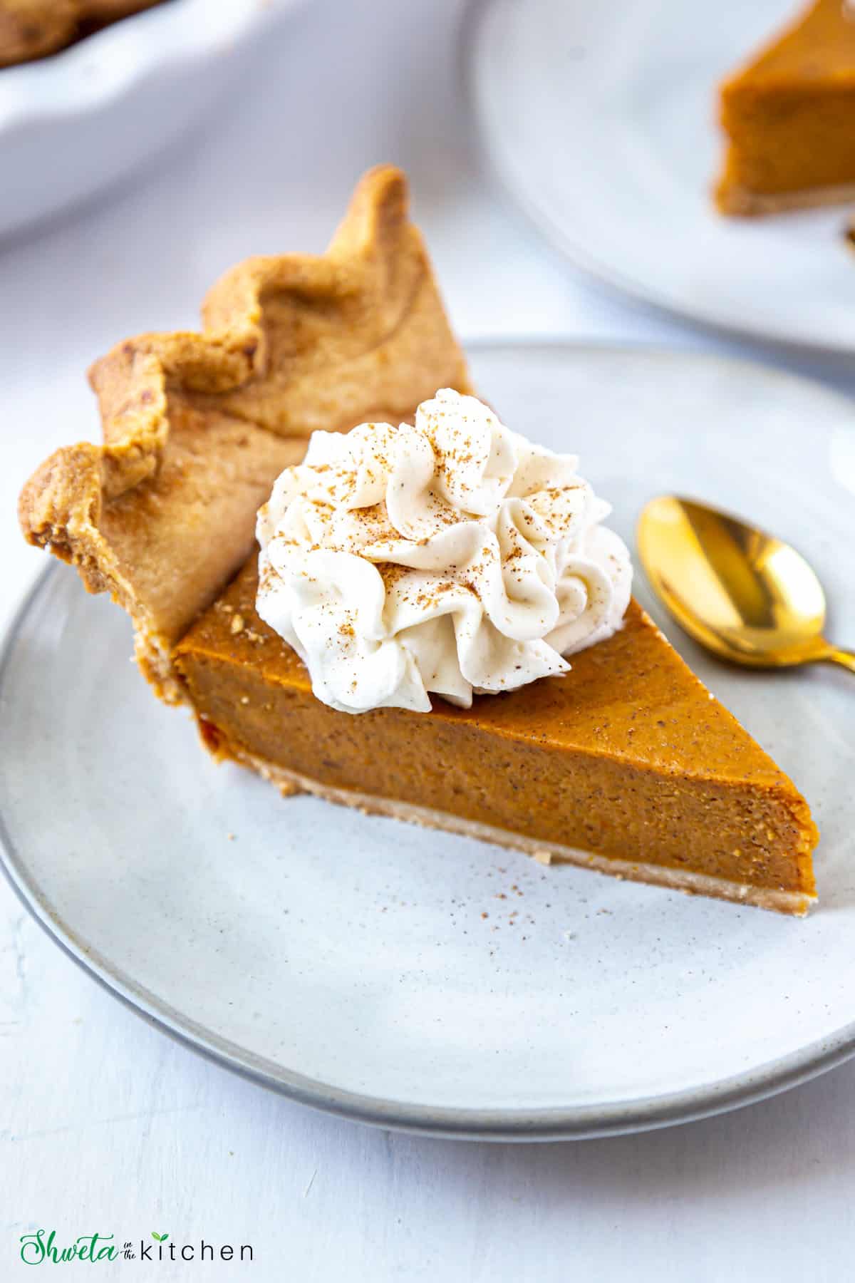 Slice of eggless pumpkin pie on a plate topped with homemade pumpkin pie spiced whipped cream