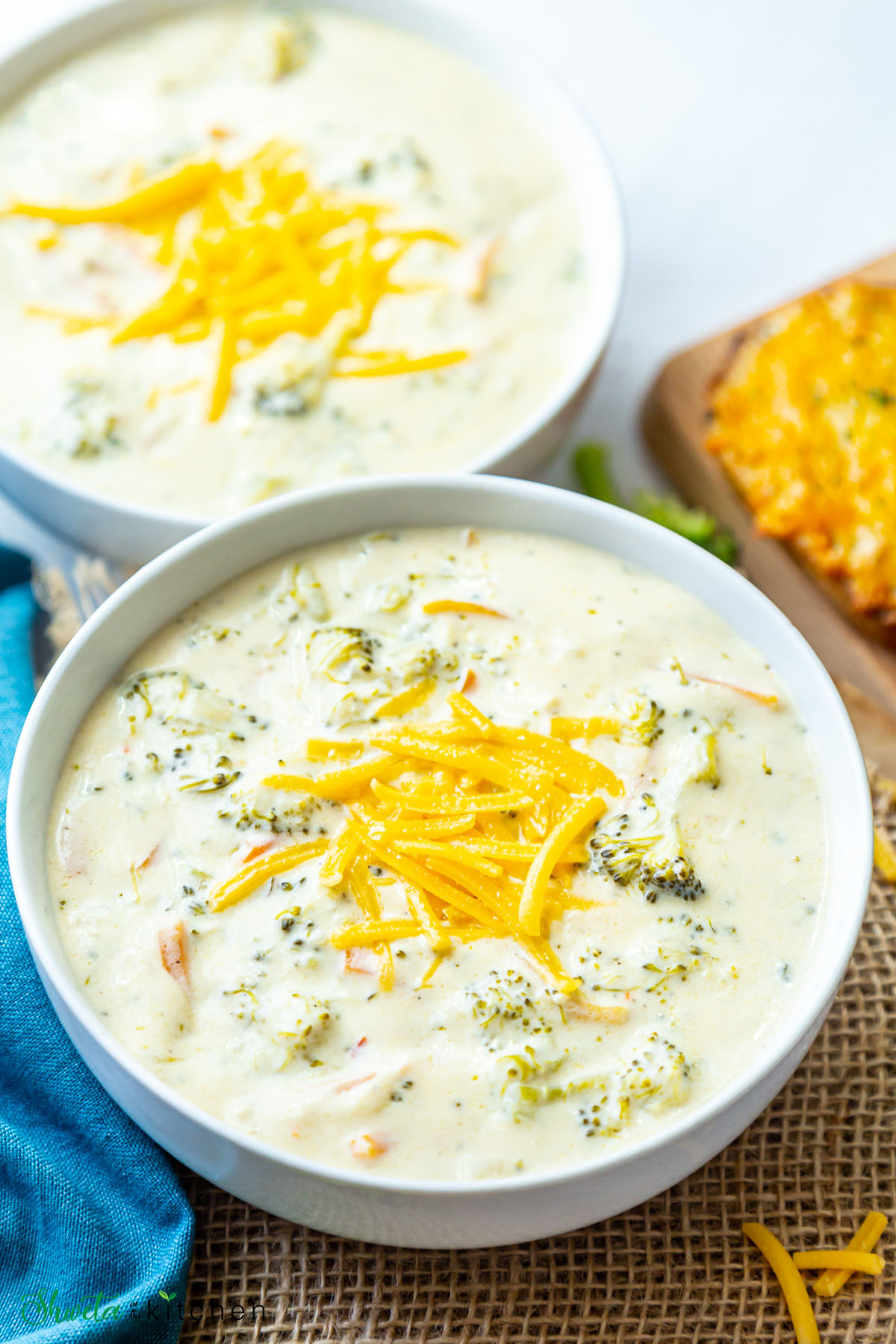 Close up of one of the two vegetarian broccoli cheddar soup bowls topped with cheese