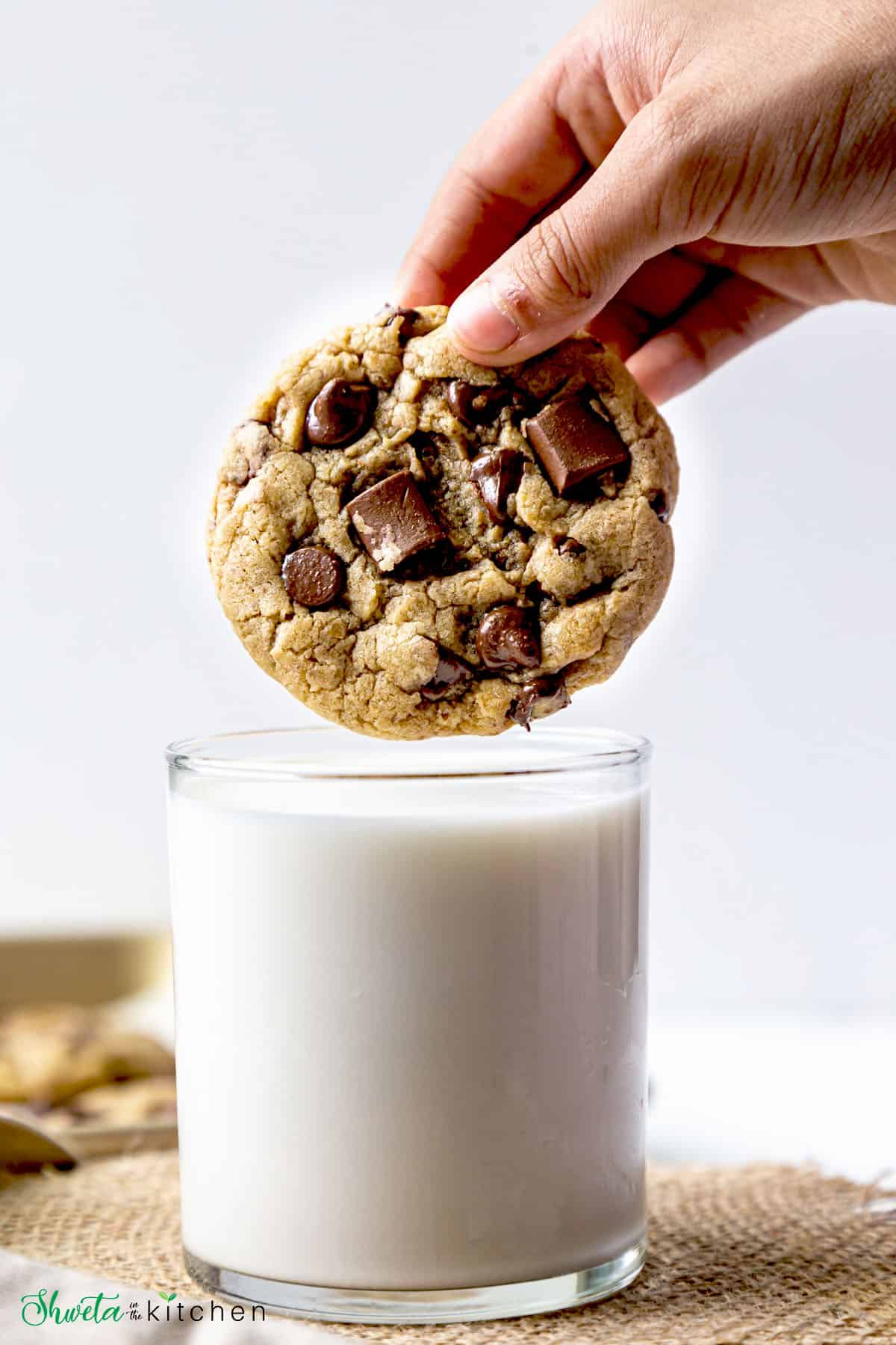 chocolate chip cookie about to be dipped in glass of milk