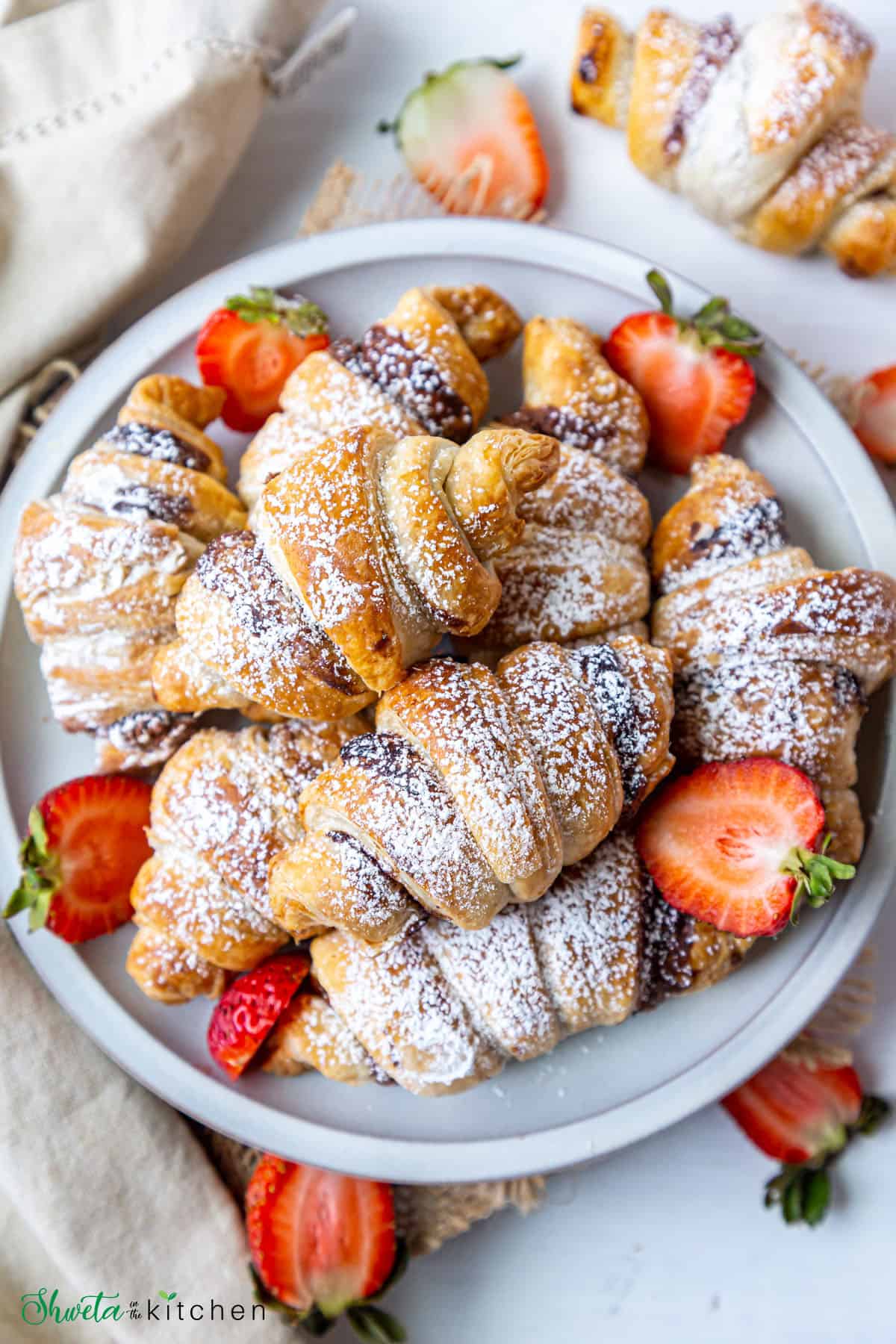 Top view of Nutella filled croissants dusted with powdered sugar piled on a plate along with cut strawberries
