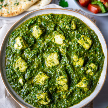 Bowl of palak paneer in center with plate of naan and salad bowl on side