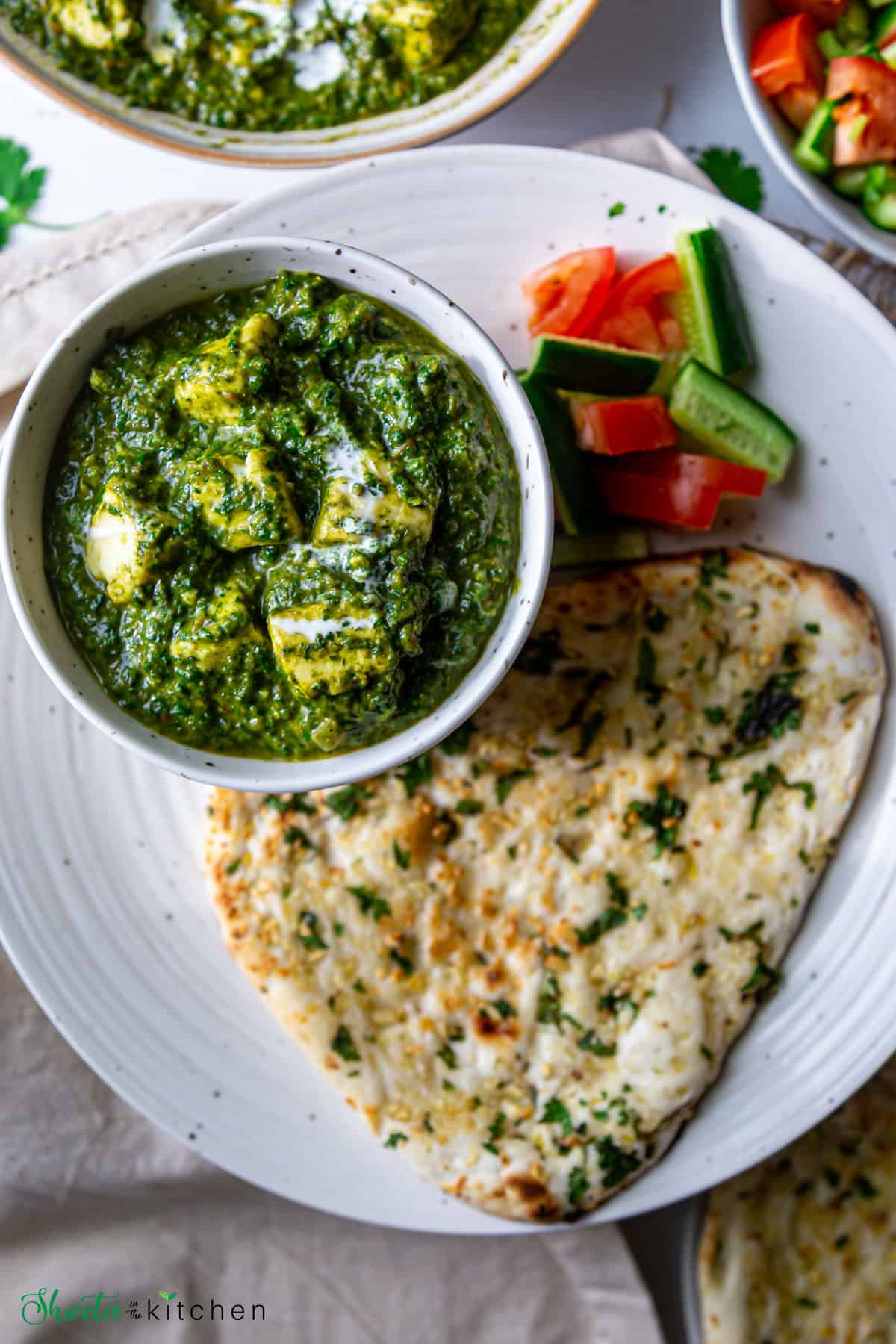 Punjabi palak paneer served in a bowl placed on a plate with naan and salad