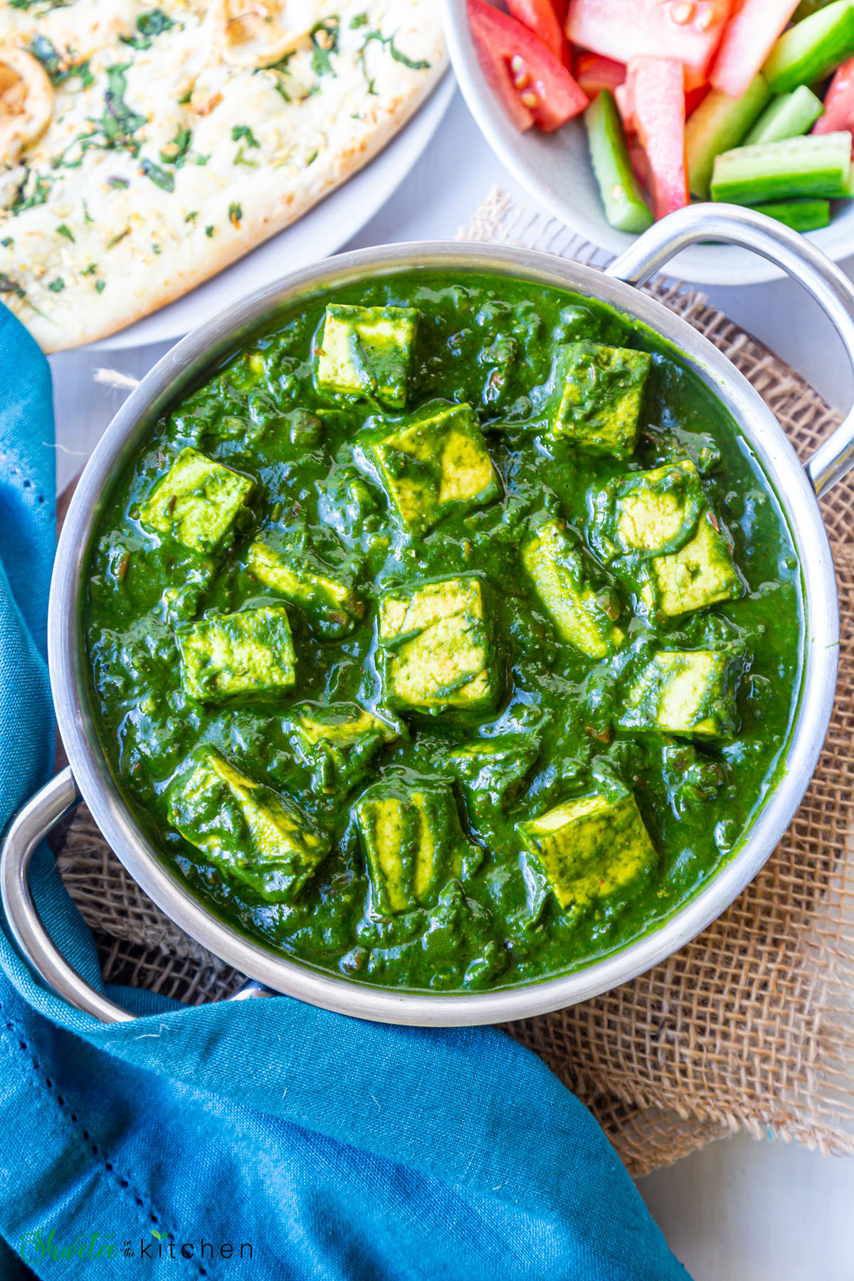 Small pan of palak paneer in center with plate of naan and salad bowl on side