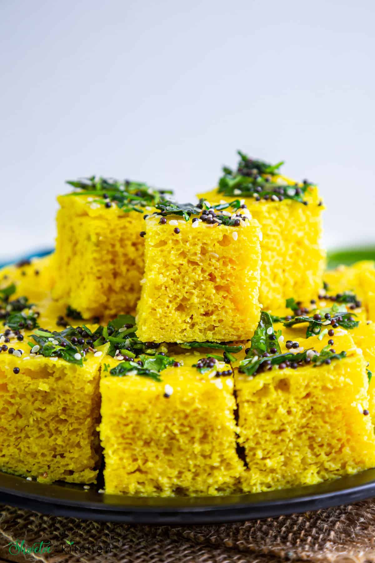 Yellow Khaman Dhokla pieces stacked on top of a black plate