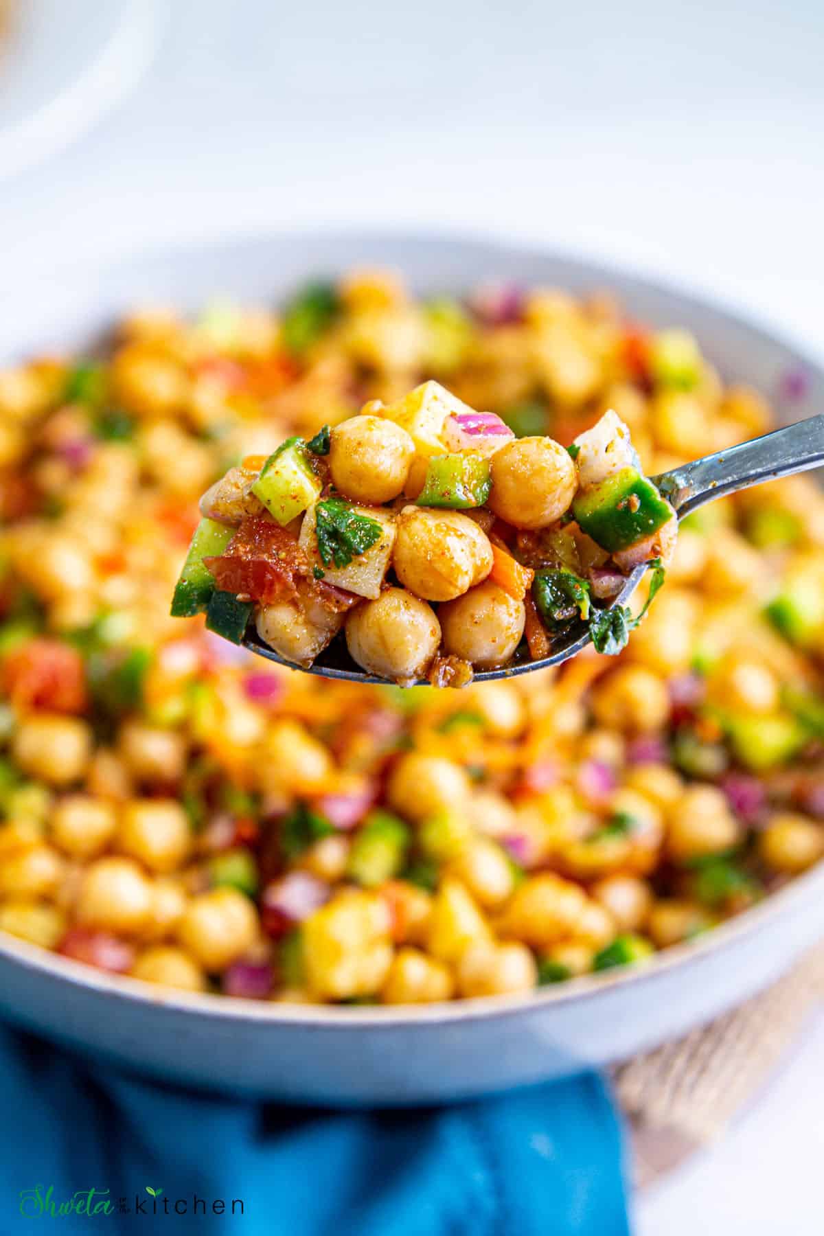 Side angle shot of spoon full of chana salad with bowl in background