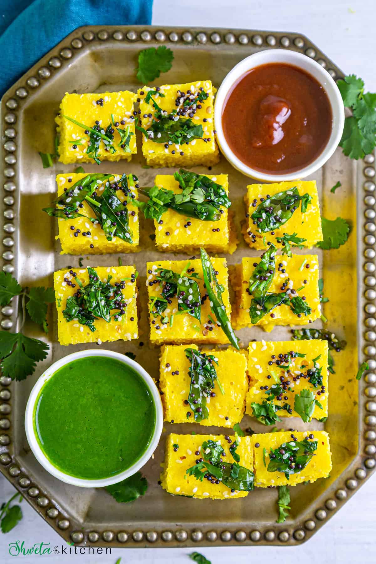 Khaman Dhokla pieces placed on a rectangle platter with sweet and green chutney on side
