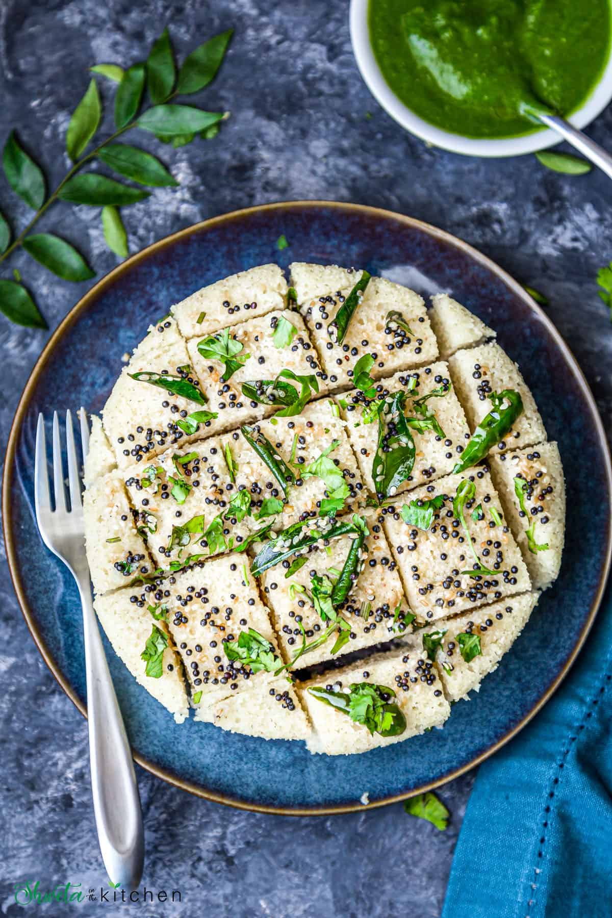 top view of Rava dhokla with tempering cut into pieces and placed on blue plate