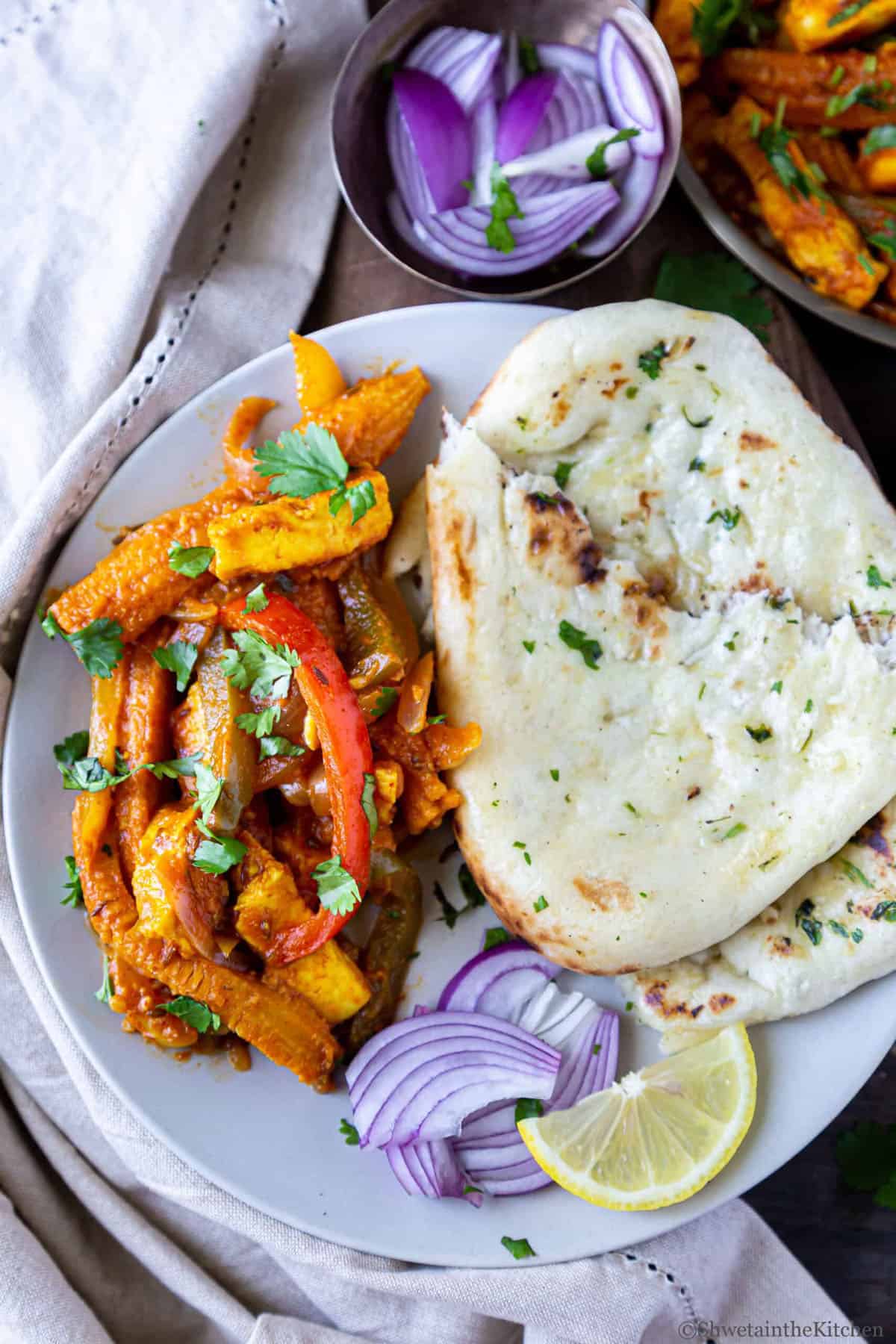 Paneer Jalfrezi, naan, sliced red onion and slice of lemon on a plate