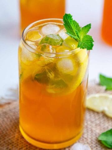 Lemon iced tea served in a tall glass with ice cubes, and lemon slices, garnished with mint leaves