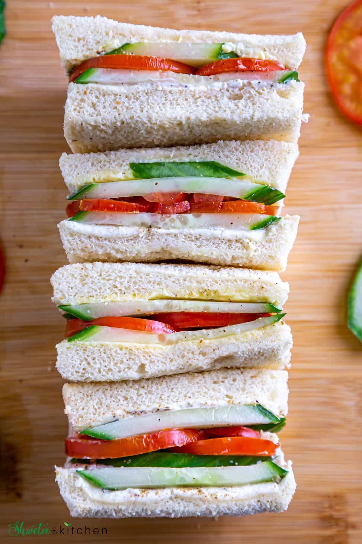 Top view of cucumber and tomato sandwiches placed inline on a wooden board