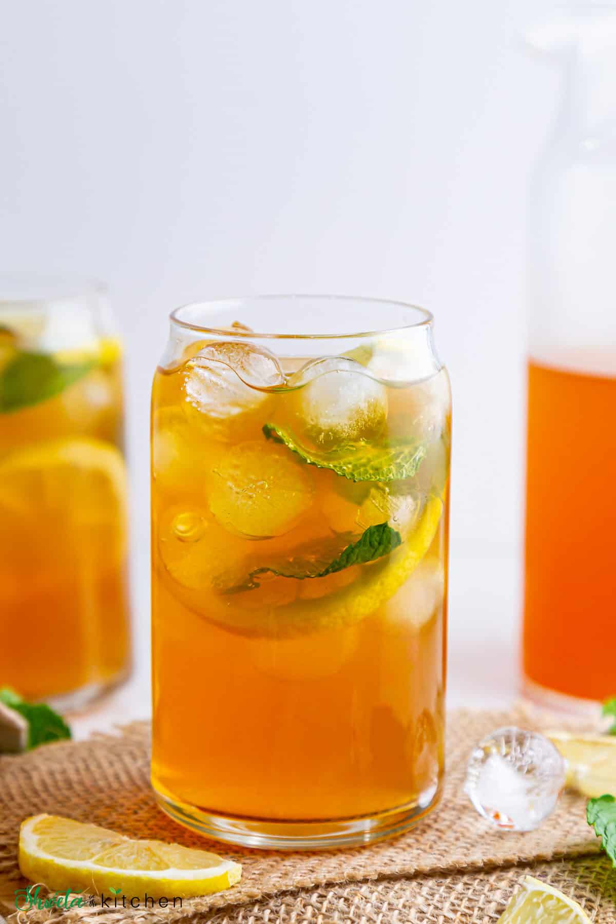 lemon iced tea served in a tall glass with ice cubes, lemon slices, and mint leaves