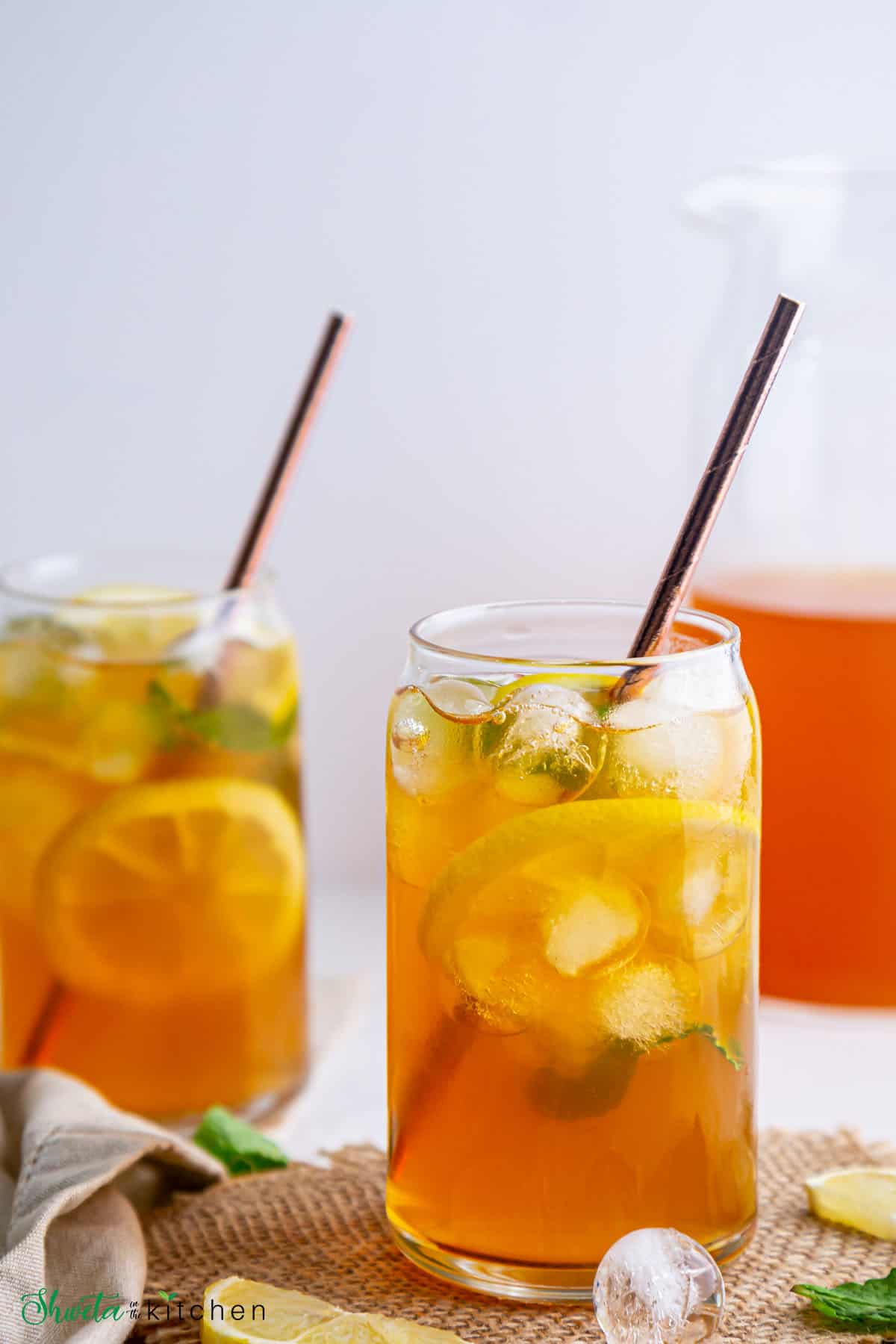 Two glasses of lemon iced tea with ice cubes, lemon slices, and straws