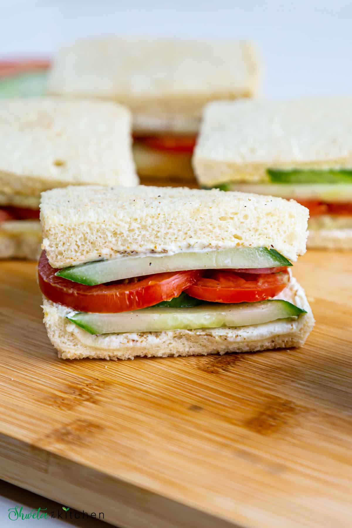 tomato and cucumber sandwich cut in half placed on wooden board