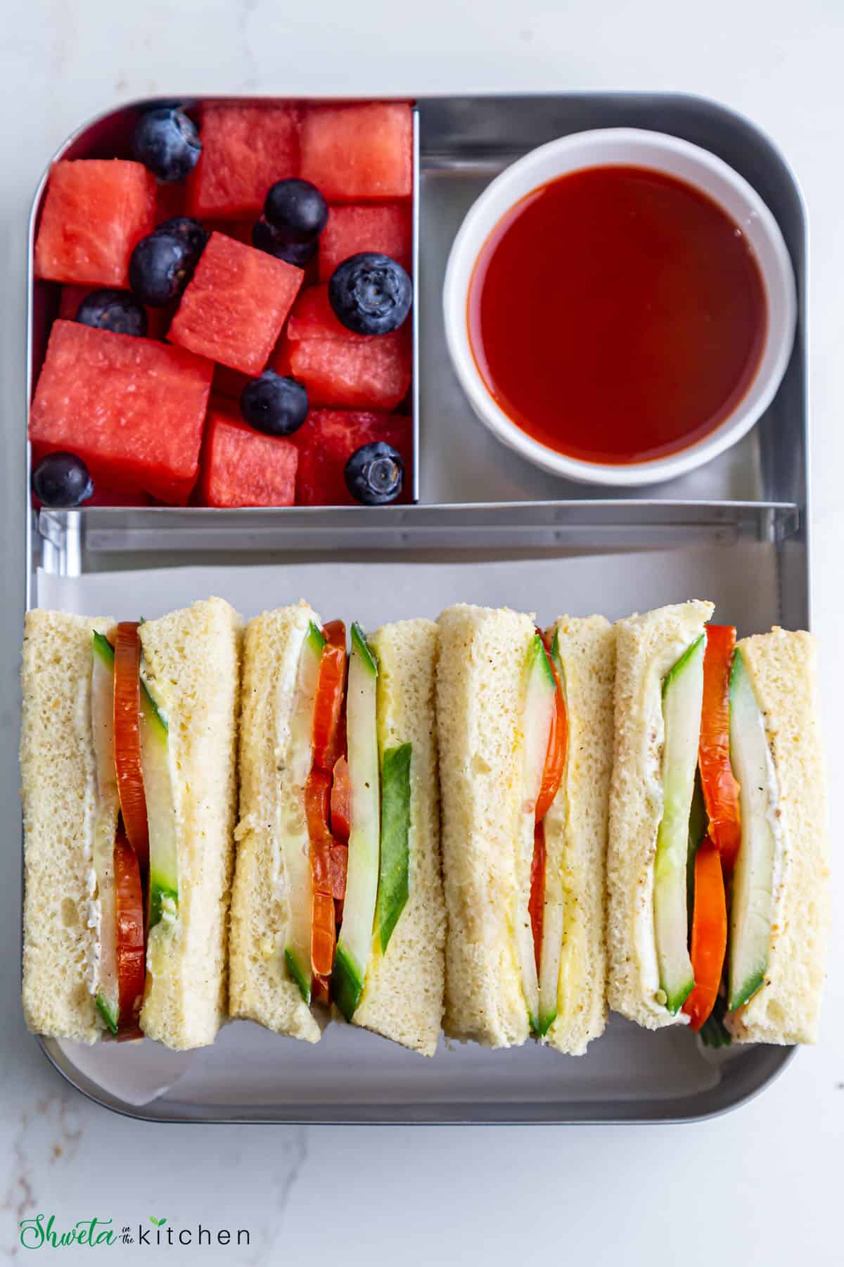 tomato cucumber sandwich packed in lunchbox with fruits and ketchup